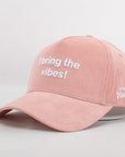 Pink cap with 'I bring the vibes!' text on a light gray background