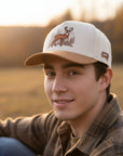 Man wearing a cap with a deer design in a field during sunset