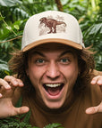 Person wearing a cap with a dinosaur design in a forest setting