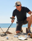 Man on a beach with a metal detector and golf balls