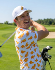 Man laughing mid-swing on the golf course wearing The Dino Nugget golf polo and Dino Nugget hat