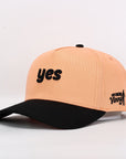 Two-tone peach and black cap with 'yes' text on a light gray background