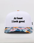 White cap with floral brim and 'At least I look good' text on a white background