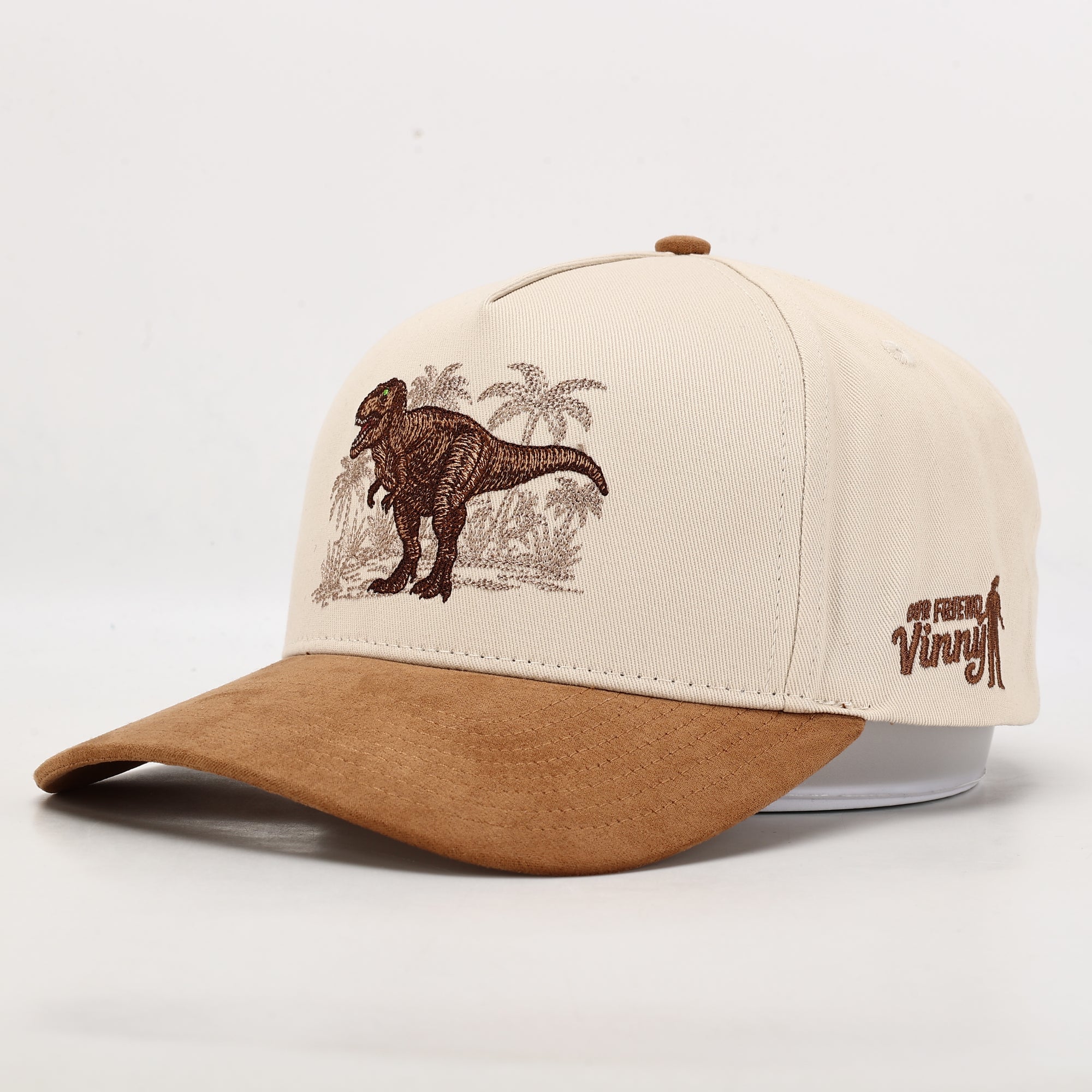 Beige and brown cap with a dinosaur and palm tree design on a white background