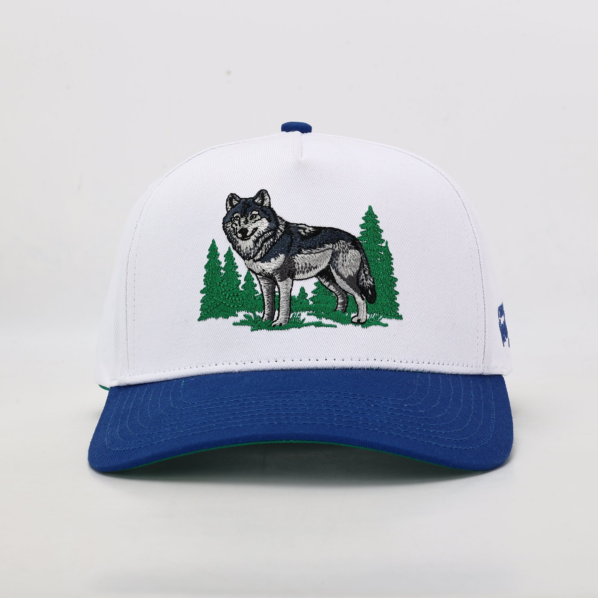 White cap with blue brim featuring a wolf and trees design on a white background