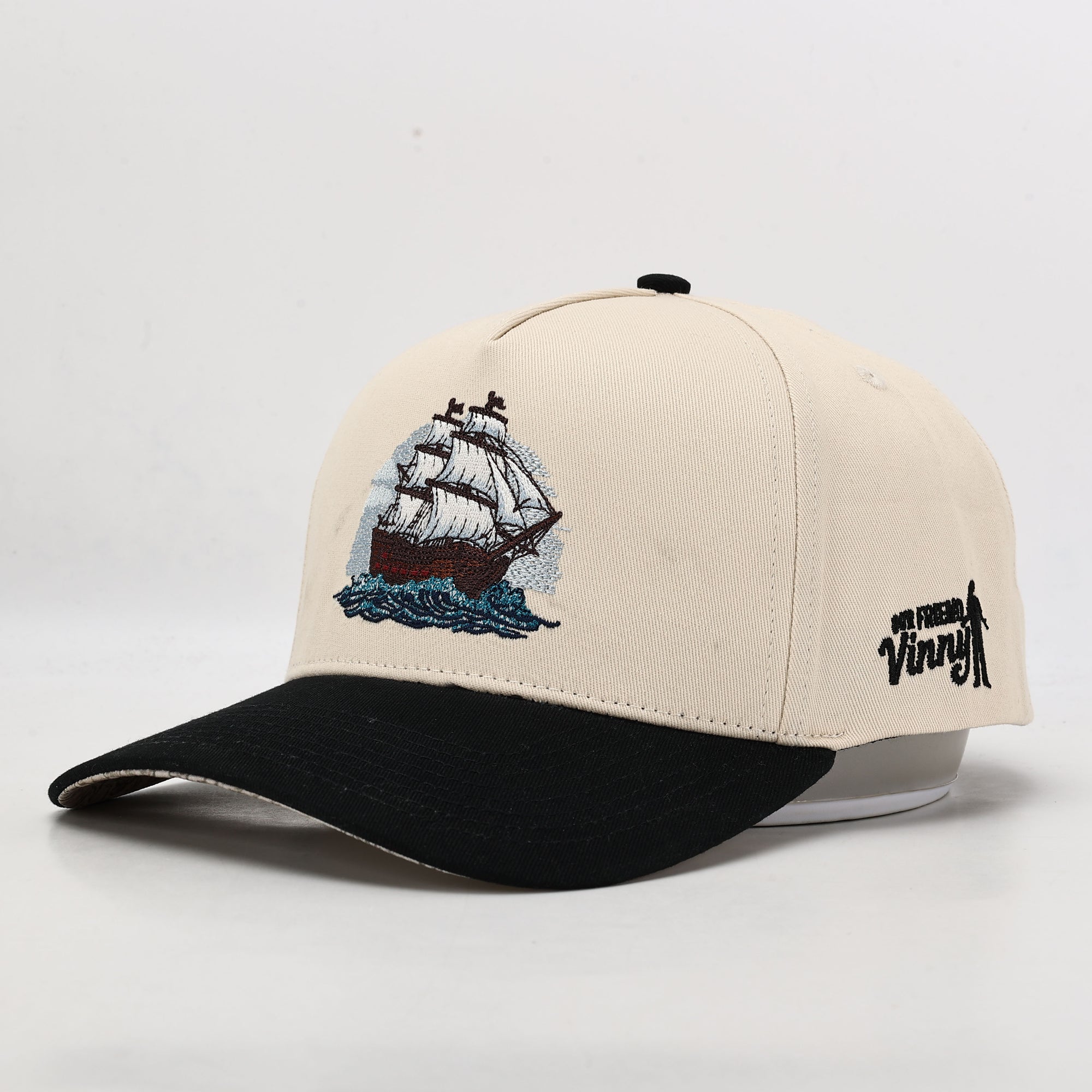 Beige cap with black brim and ship embroidery on a white background