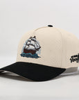 Beige cap with black brim and ship embroidery on a white background