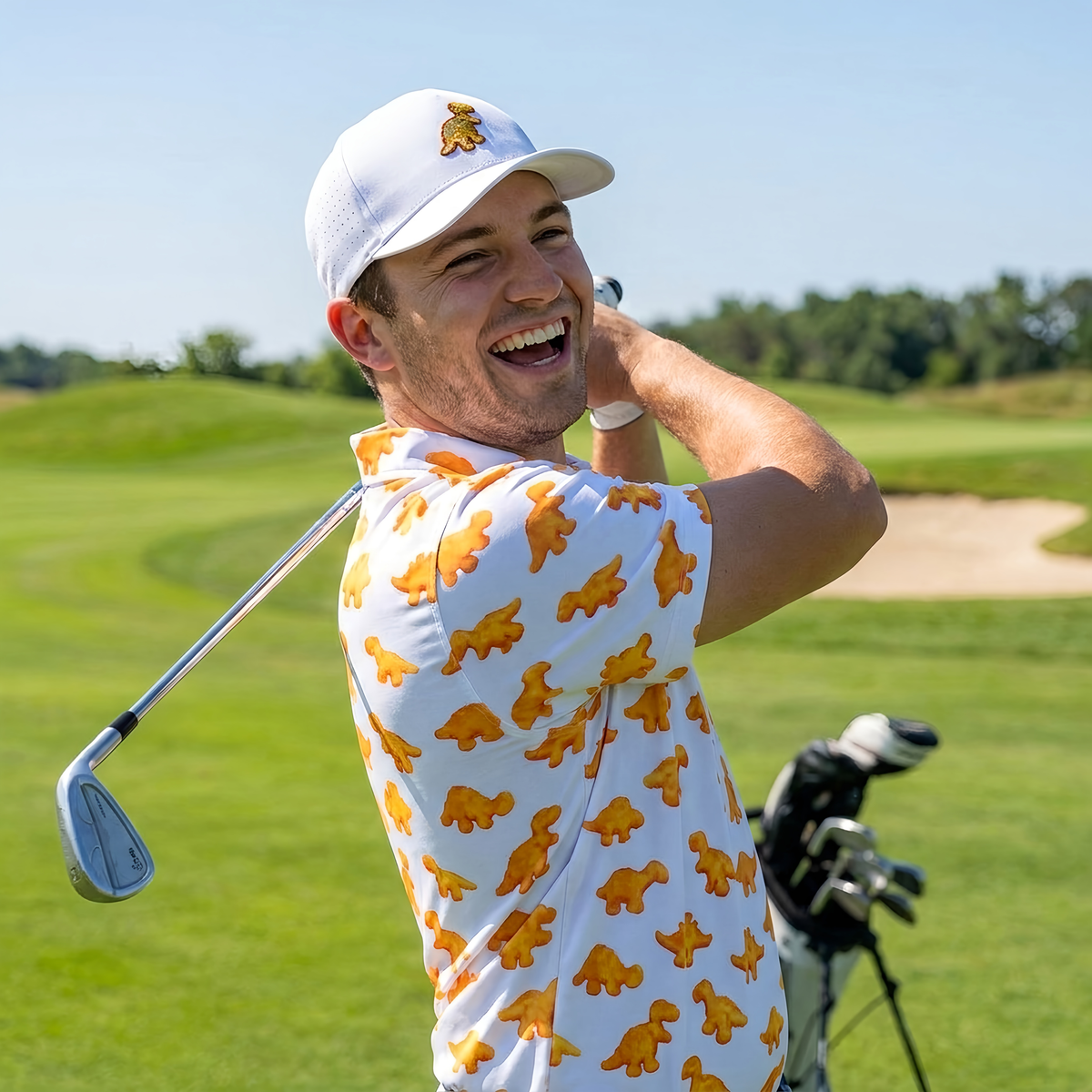 Man laughing mid-swing on the golf course wearing The Dino Nugget golf polo and Dino Nugget hat