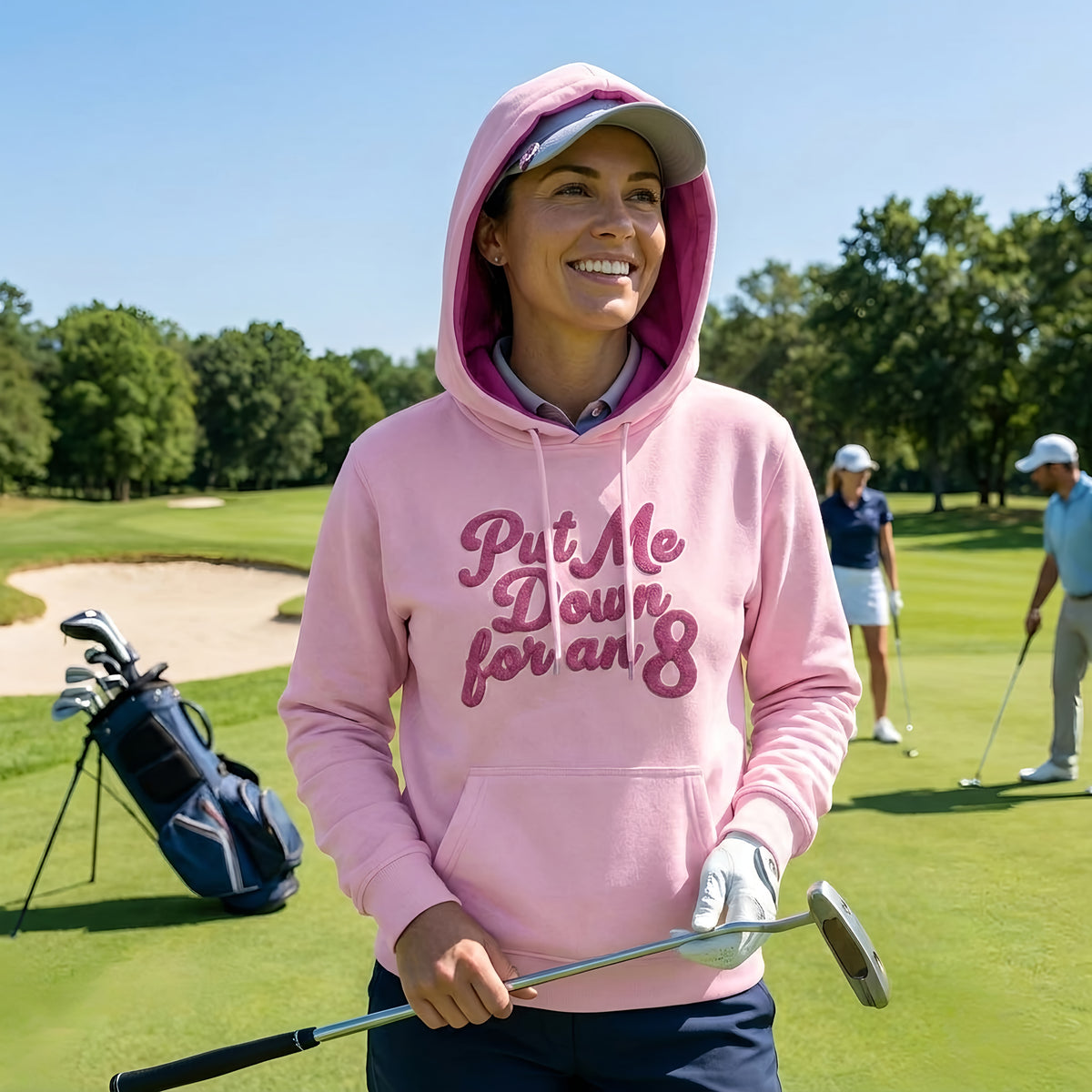 Smiling golfer wearing the pink Put Me Down for an 8 hoodie with the hood up on a sunny golf course