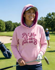Smiling golfer wearing the pink Put Me Down for an 8 hoodie with the hood up on a sunny golf course