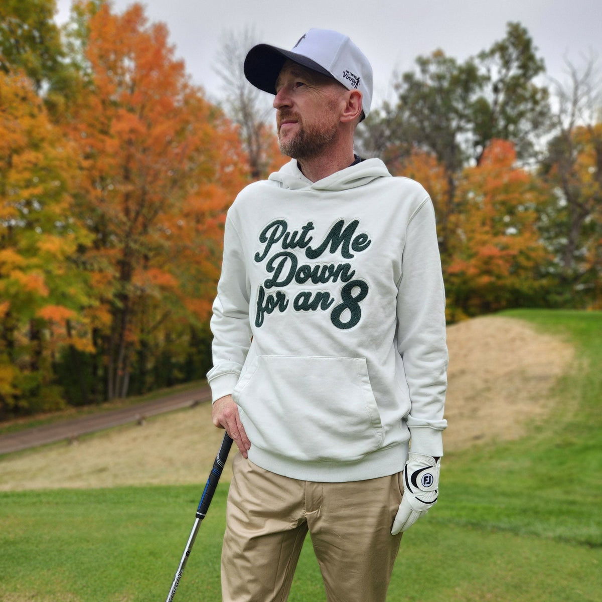 Golfer wearing the white Put Me Down for an 8 hoodie on a fall golf course