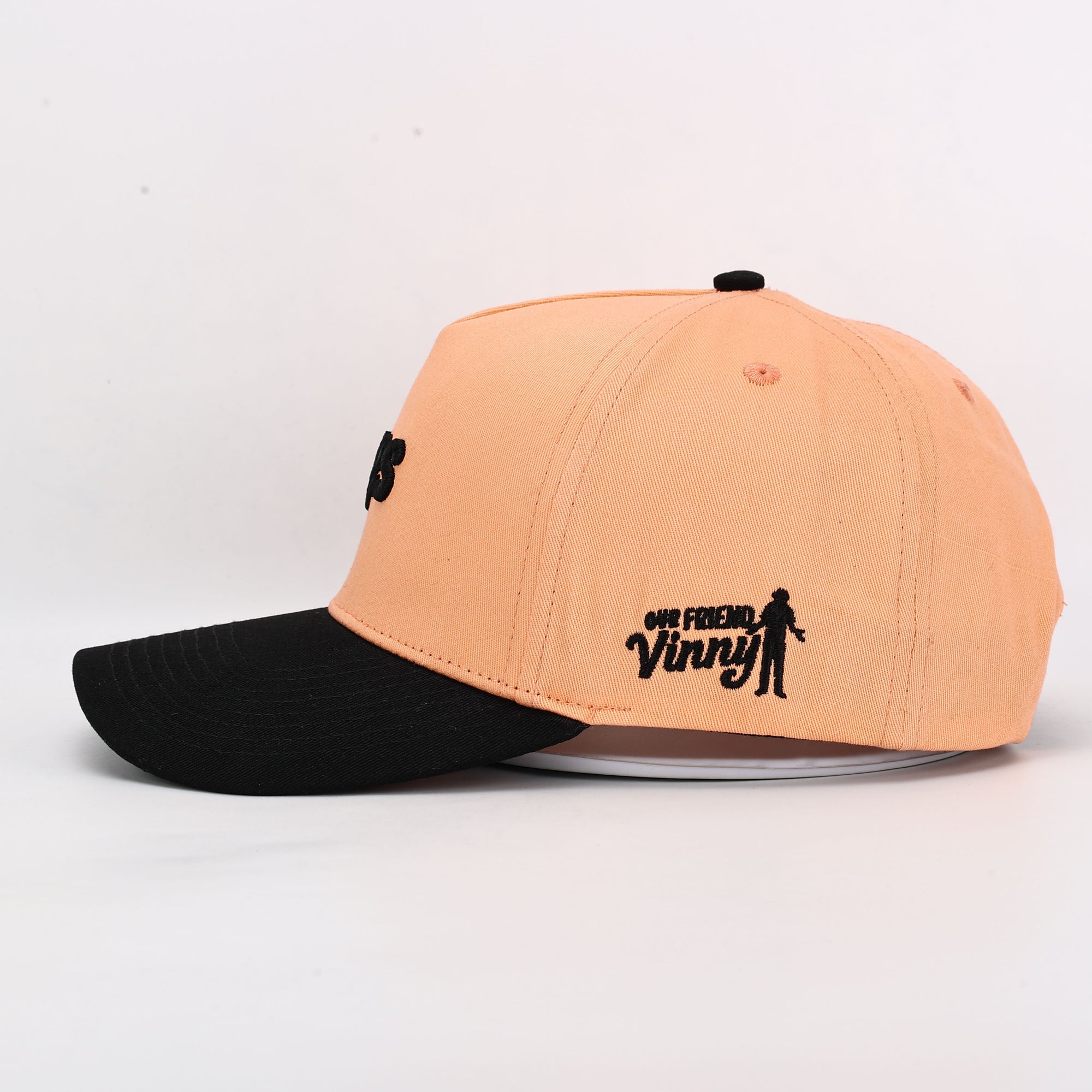 Two-tone peach and black cap with 'Our Friend Vinny' text on a light gray background