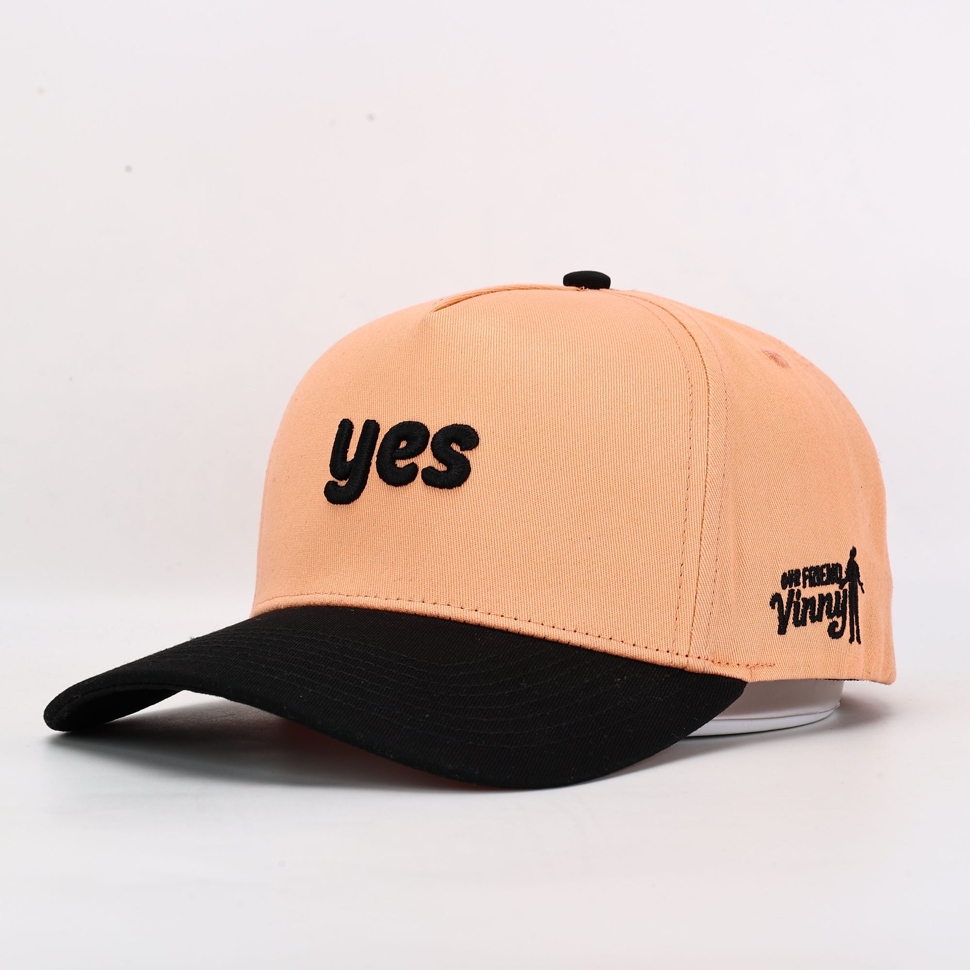 Two-tone peach and black cap with 'yes' text on a light gray background